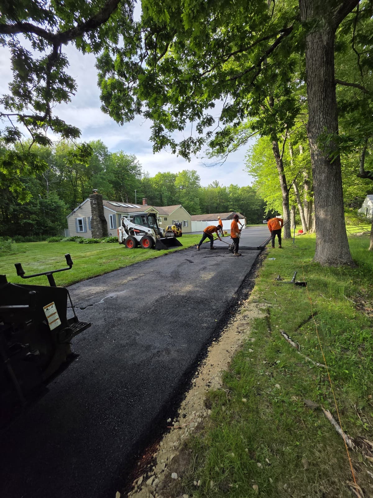 Skid steer grading a new asphalt driveway on a wooded lot